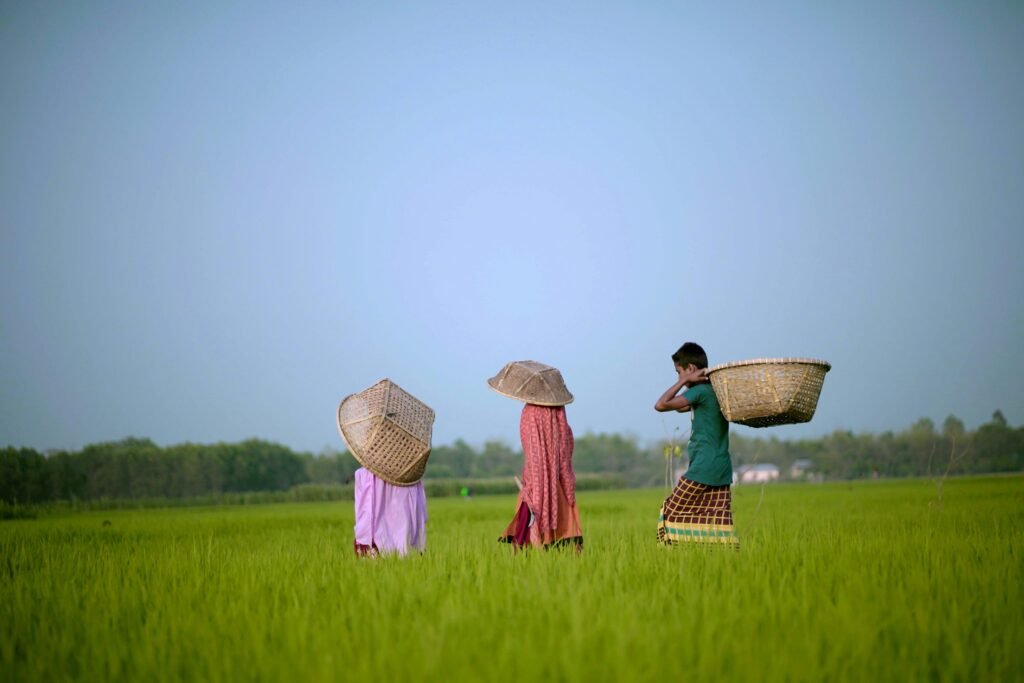 Farmers carrying baskets through vibrant green fields in a serene rural landscape.