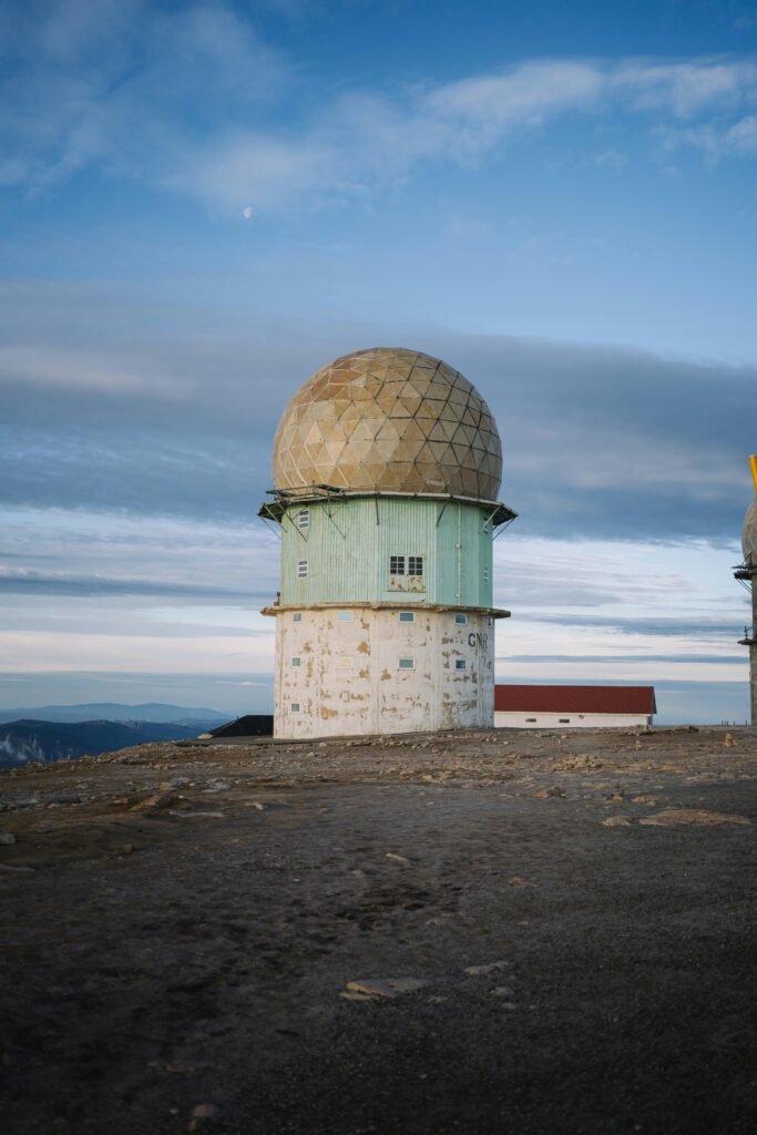 Isolated radar dome on a mountain captured during daytime under a vast sky.
