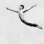 A captivating black and white photo of a male gymnast performing a dramatic leap, showcasing strength and grace.