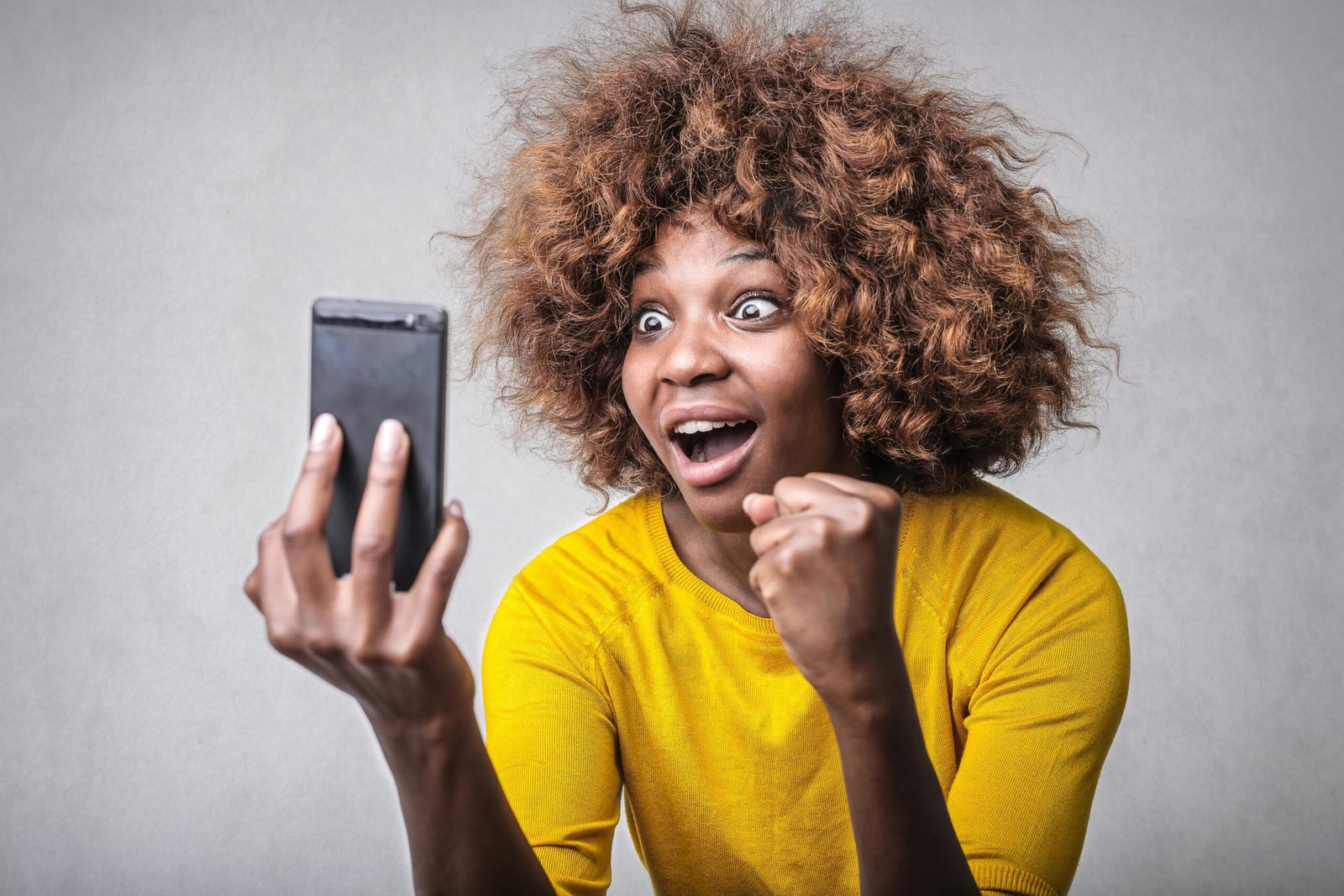 Joyful woman in yellow showing surprise and excitement at smartphone message indoors.