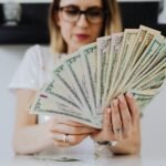 Close-up of a woman holding and fanning U.S. dollar bills indoors.