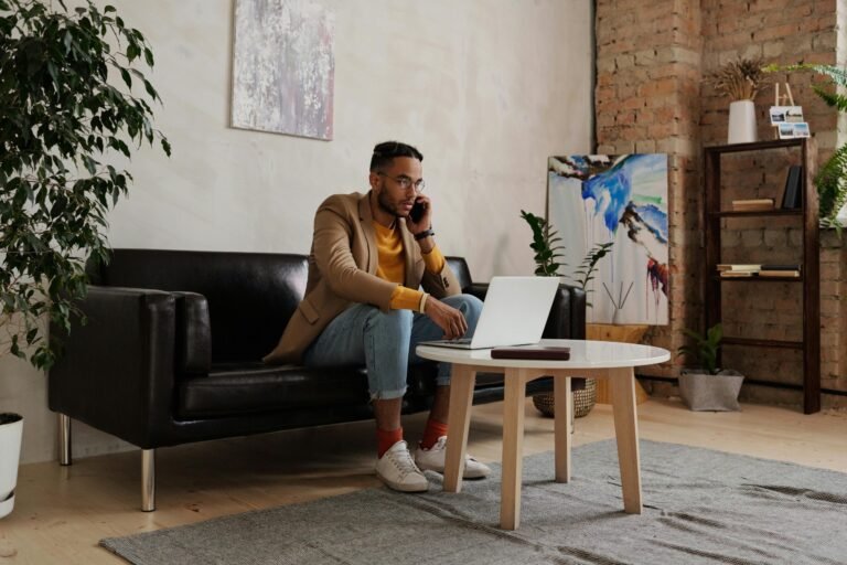 Adult man multitasking on phone and laptop in a cozy home office setting.