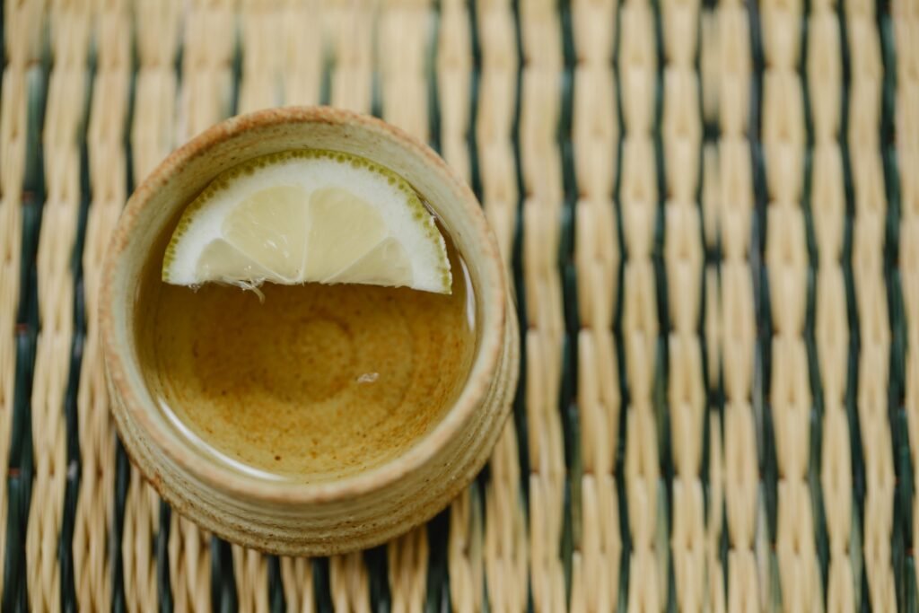 Top view of a lemon-infused hot beverage in a ceramic cup on a traditional wicker mat.