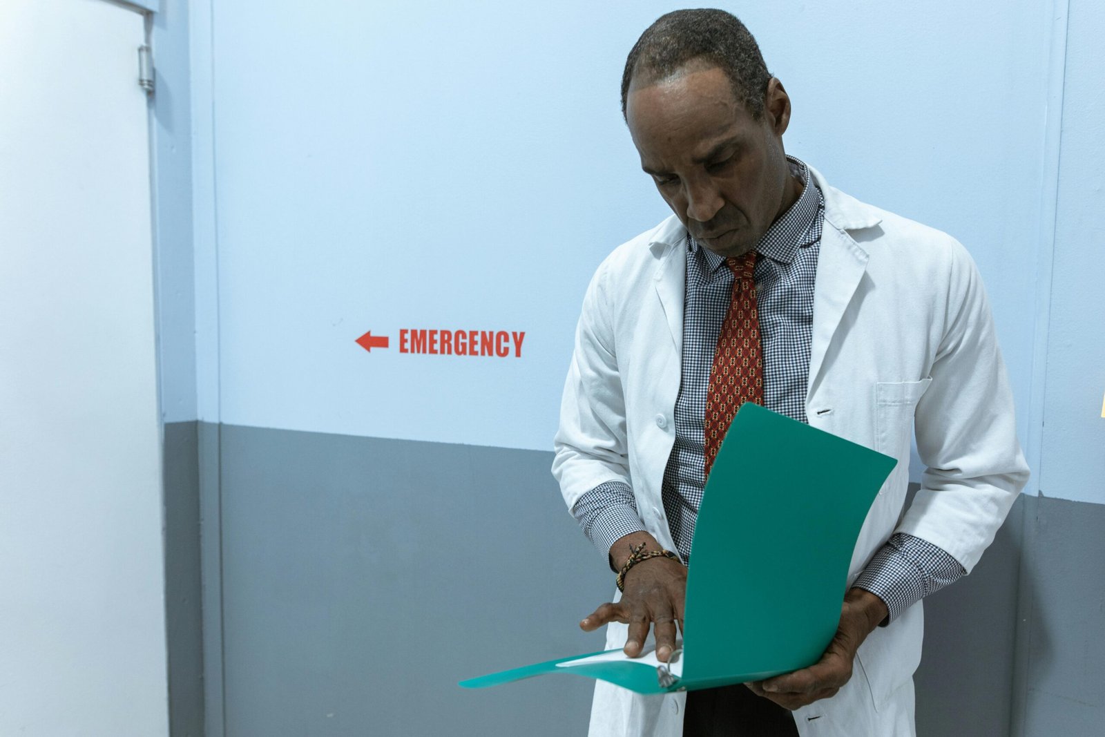 A doctor in a lab coat examines documents near the emergency room sign.