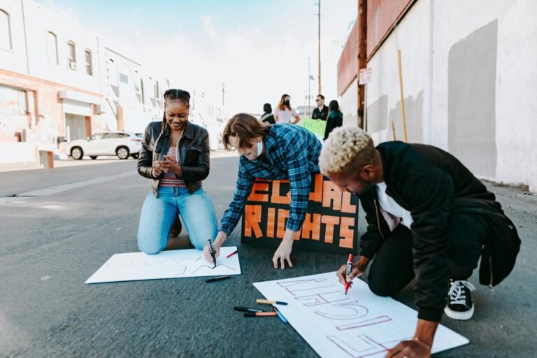 A diverse group of adults creates signs for a civil rights protest on a sunny day.