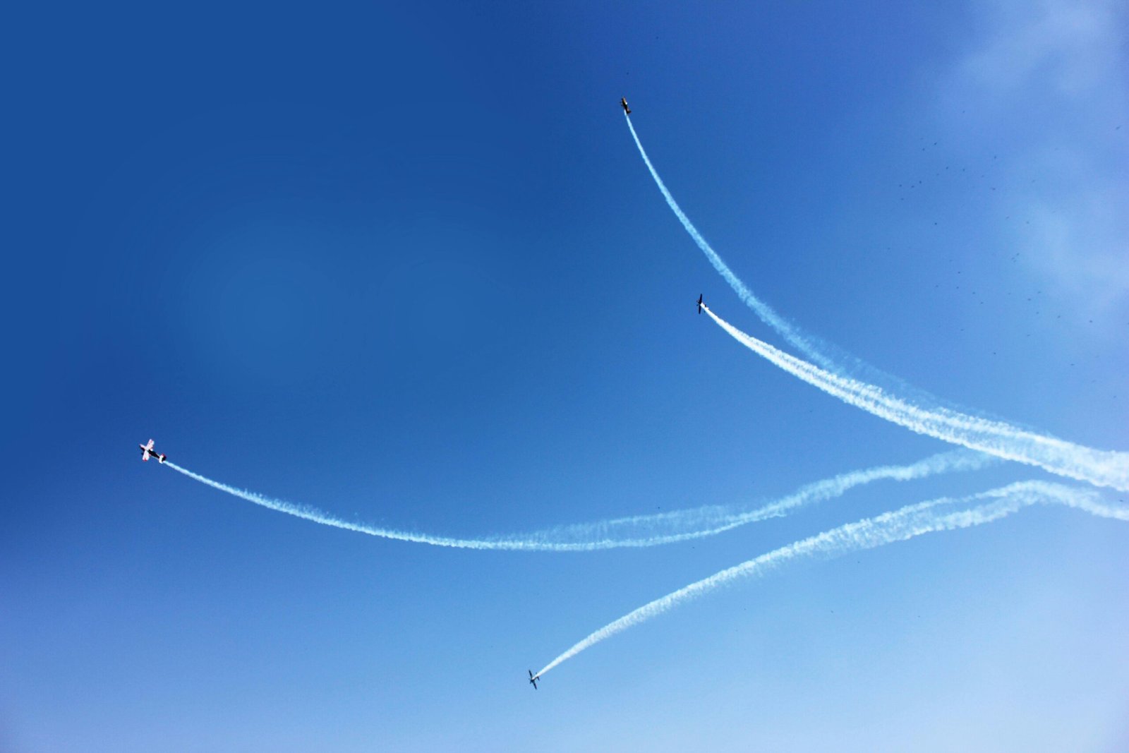 Three airplanes performing aerobatics with smoke trails against a clear blue sky.