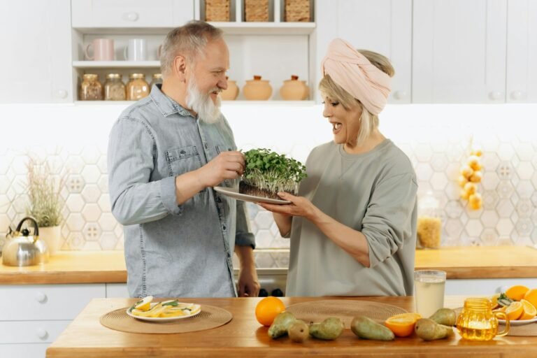 Happy senior couple smiling and holding a plate of fresh microgreens in a cozy kitchen setting.